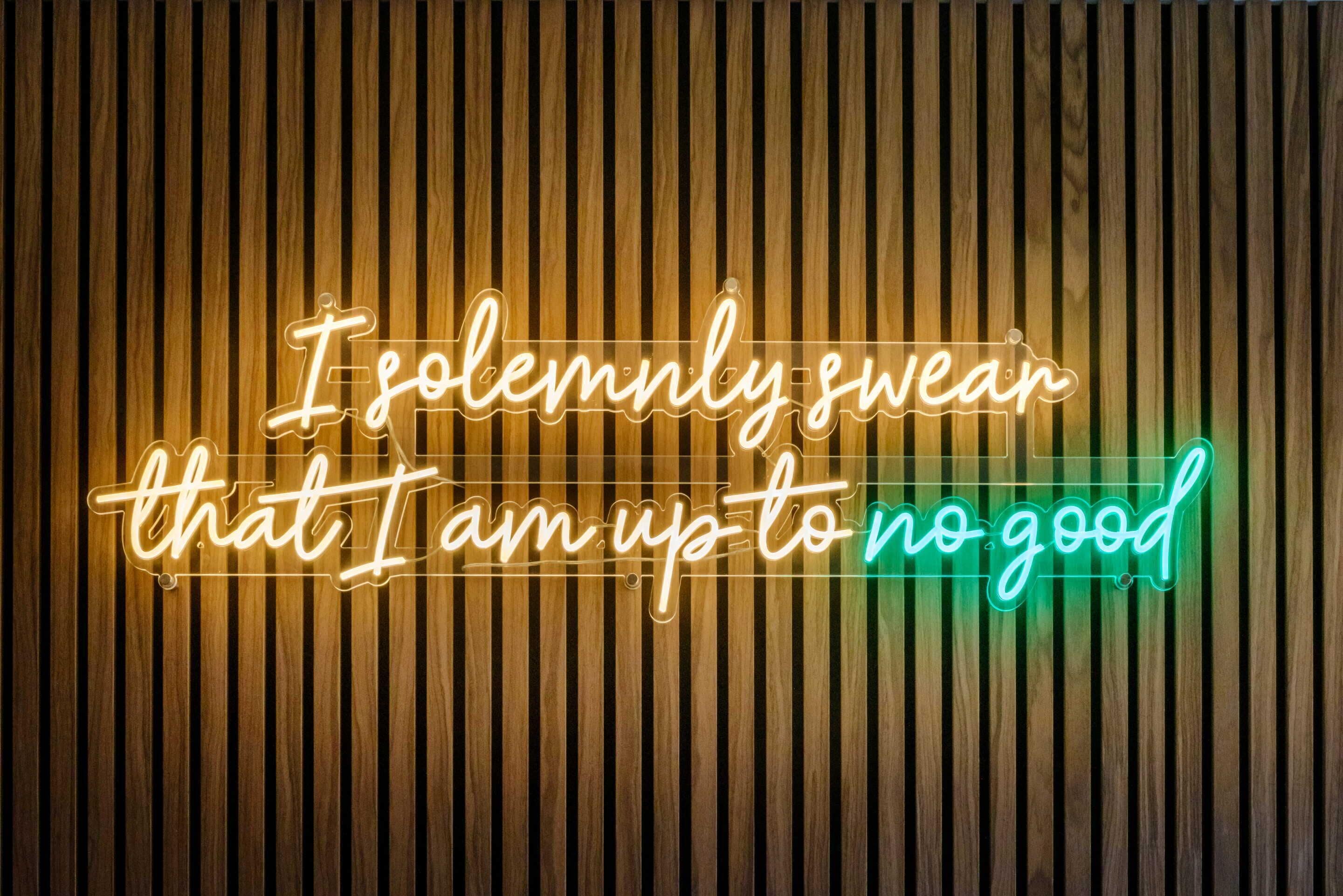 En neonskilte med teksten 'I solemnly swear that I am up to no good' mod en træbaggrund.