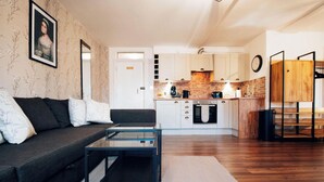 A modern living room with a sofa, coffee table, and kitchen in the background. - Ricky Road Guest House (Watford)