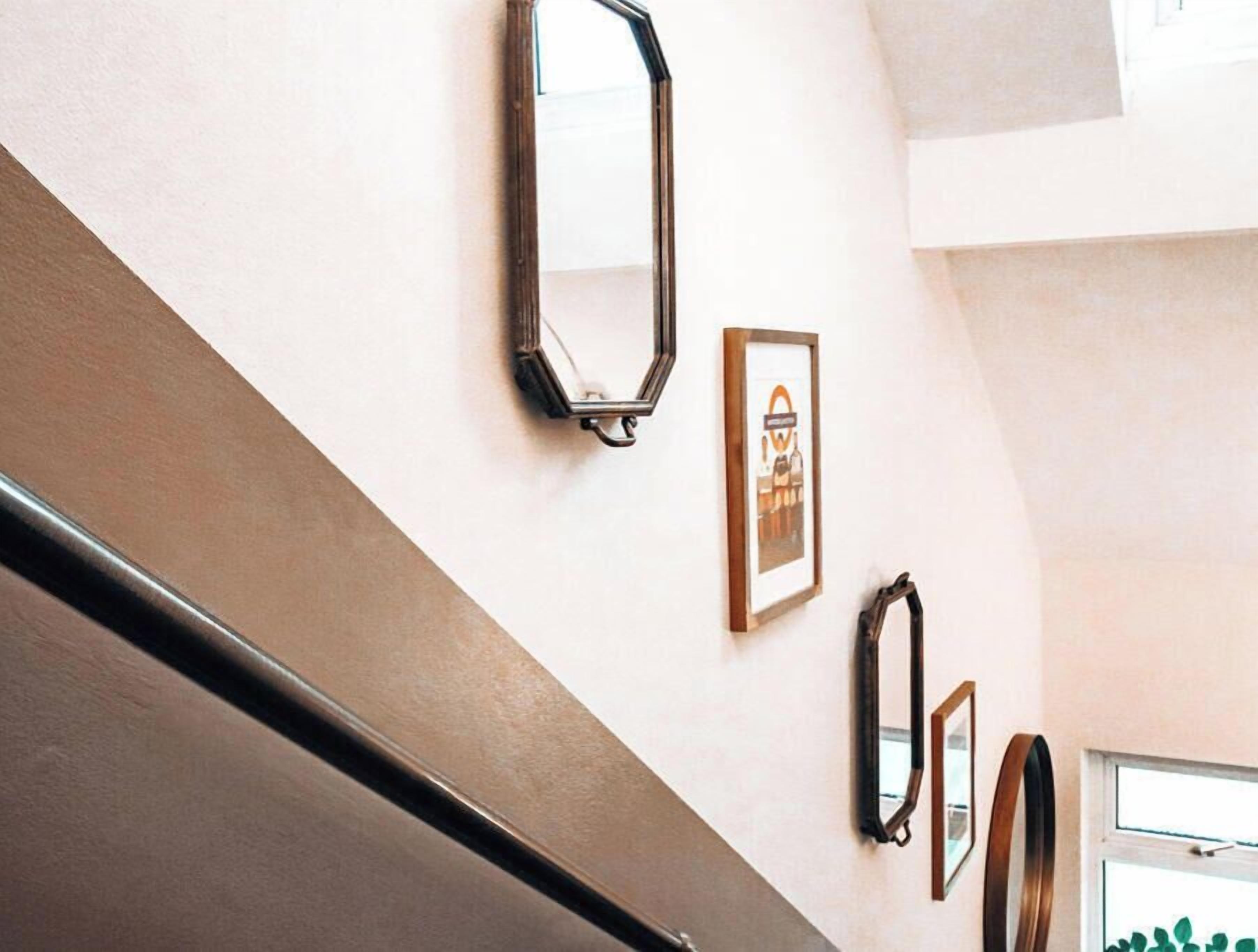 A staircase with a handrail, a wall with three framed pictures, and a window with a view of greenery.