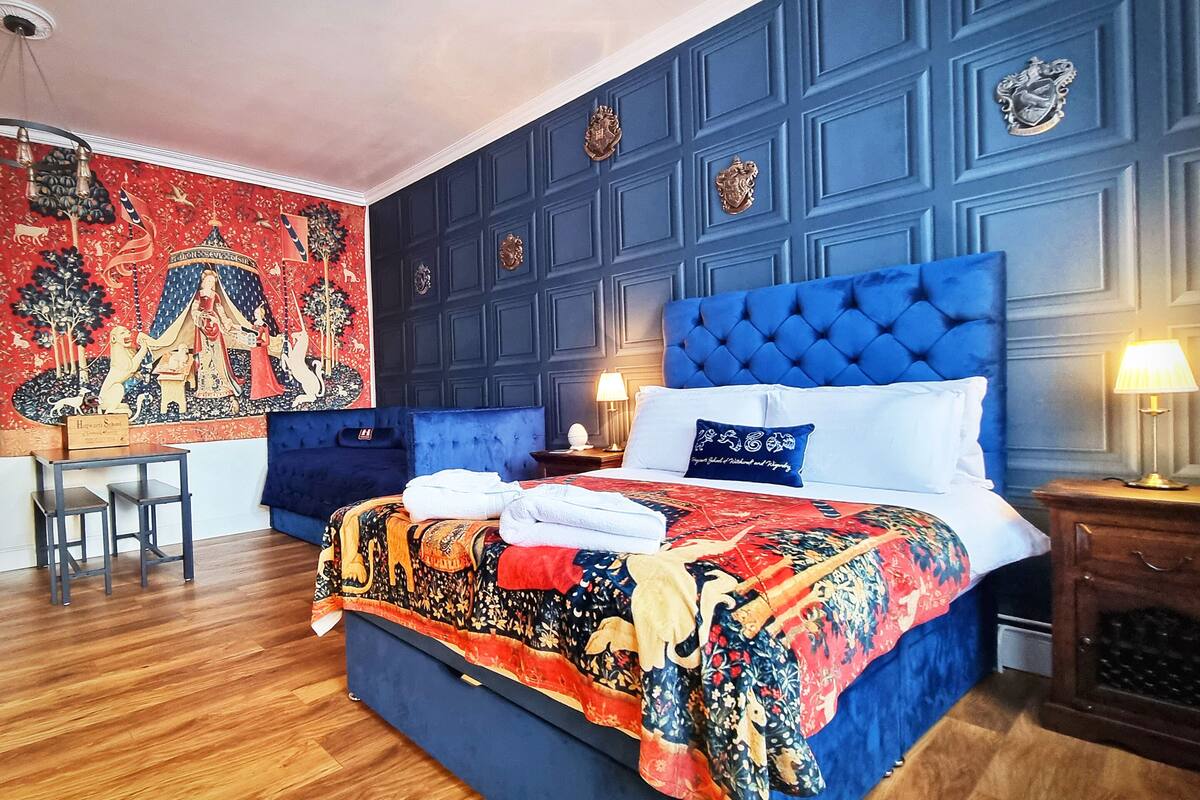 A bedroom with a large bed, a desk, and a tapestry on the wall.