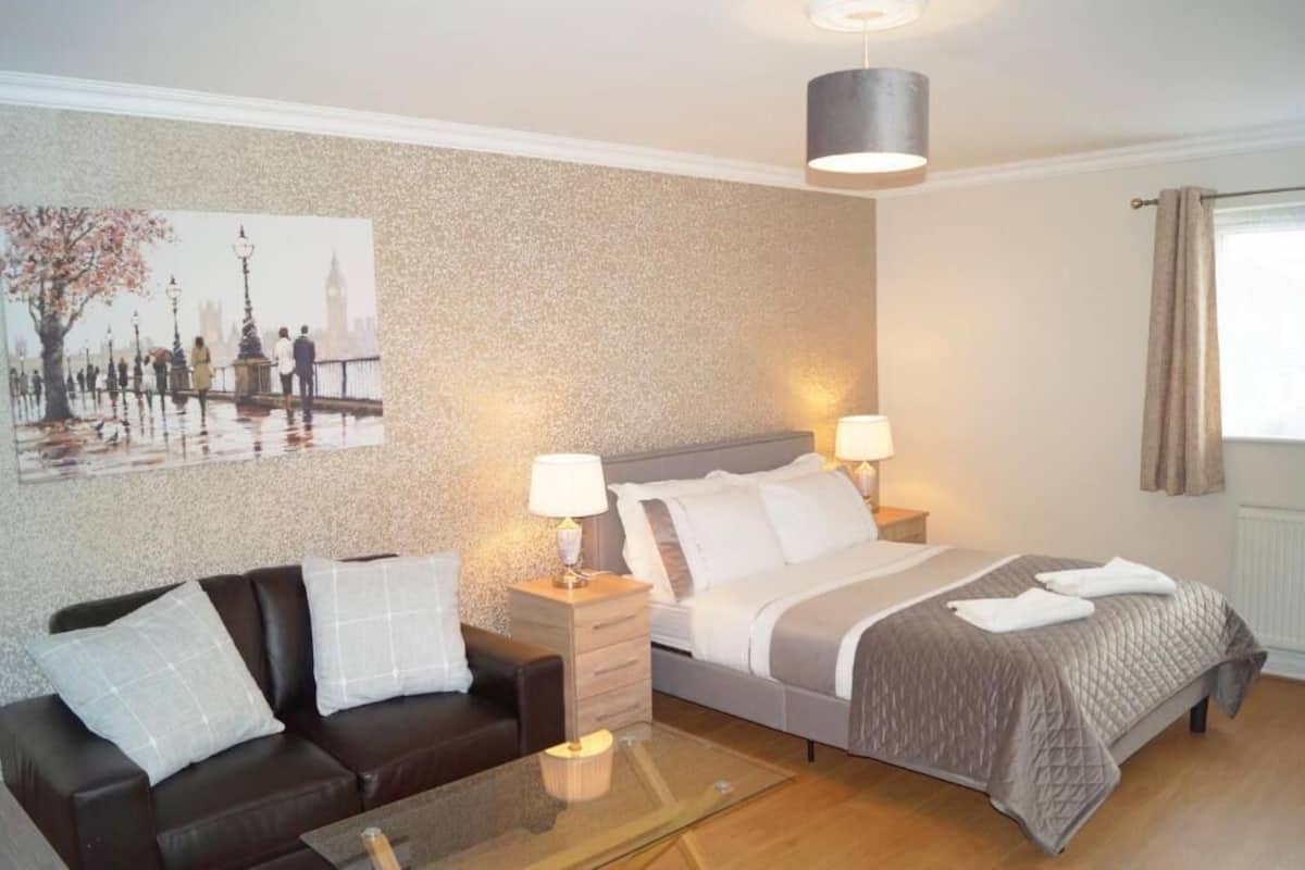 A hotel room with a bed, bedside lamps, a sofa, a coffee table, and a painting on the wall.