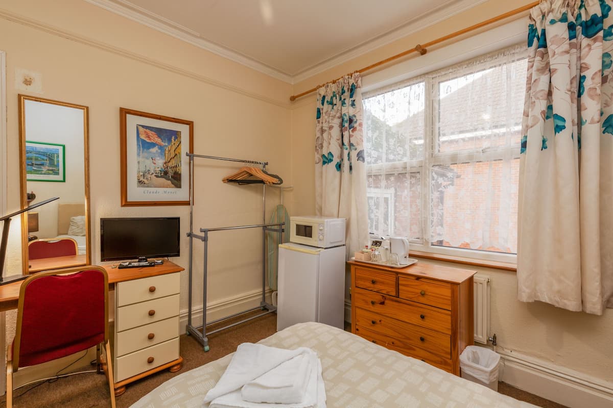 A hotel room with a bed, a desk with a chair, a television, a microwave, a dresser, and a window with curtains.