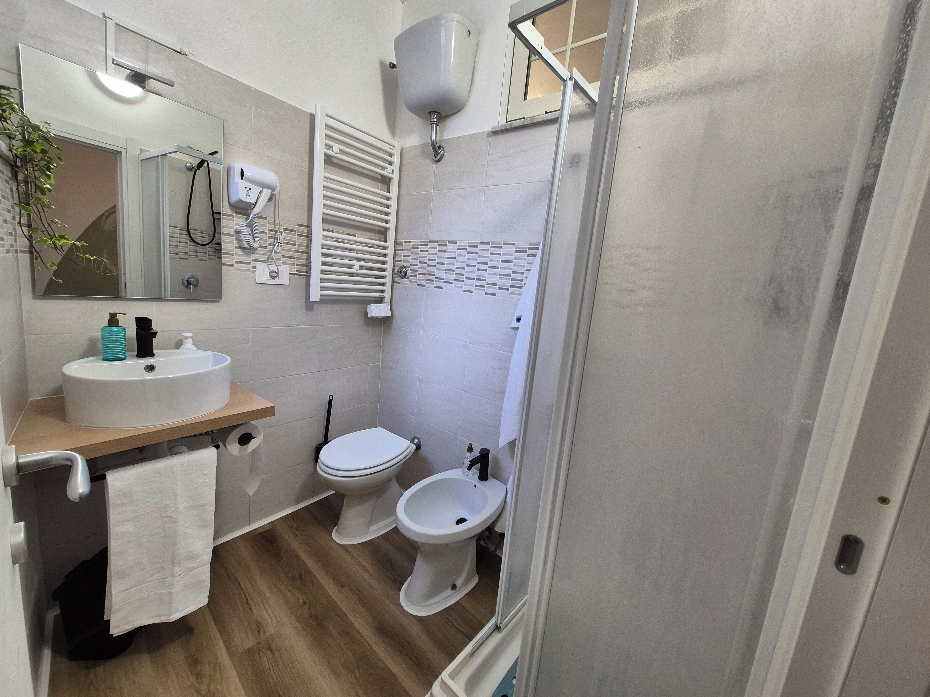 A modern bathroom with a sink, two toilets, a bidet, a mirror, and a towel rack.