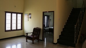 A room with a wooden chair, a staircase, and a door leading to another room. - SaiRenu Residency  (Coimbatore)