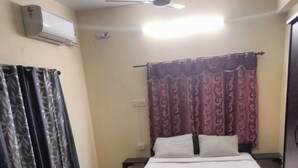 A bedroom with a bed, a ceiling fan, an air conditioner, and curtains. - SaiRenu Residency  (Coimbatore)