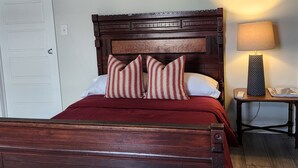 A wooden bed with a headboard, a bedside table with a lamp, and a white door. - Modern apartment overlooking historic downtown Elloree, SC. (Elloree)