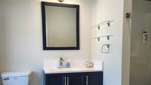 A bathroom with a toilet, dark blue vanity, a mirror, and a glass shower enclosure. - Modern apartment overlooking historic downtown Elloree, SC. (Elloree)