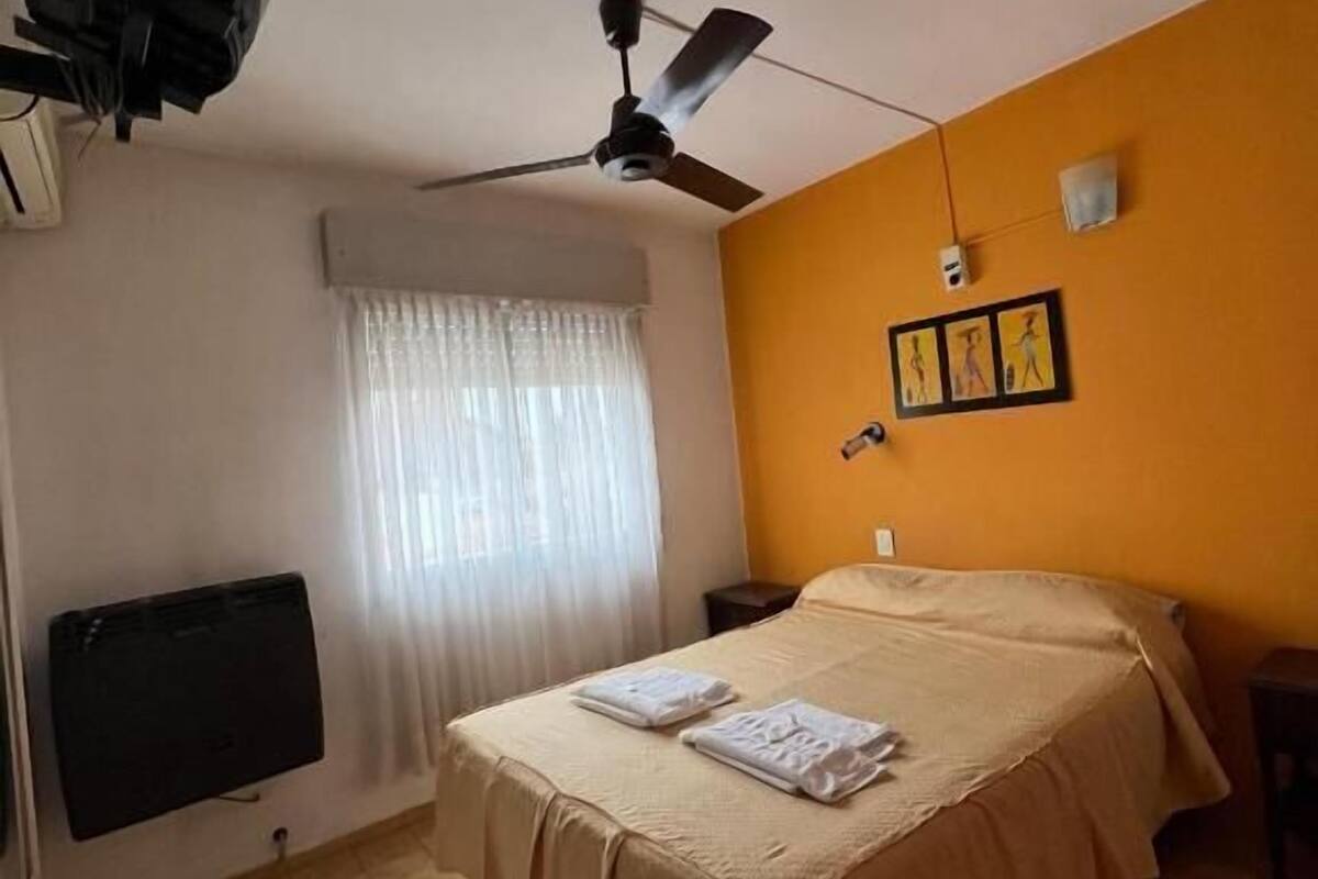 A hotel room with a bed, a ceiling fan, a flat-screen TV, and a window with curtains.