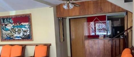 A spacious living area with a tiled floor, wooden furniture, a ceiling fan, and a painting on the wall.