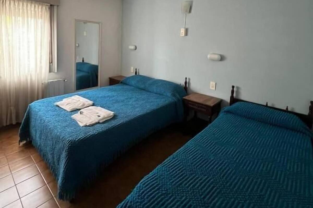 A hotel room with two beds, a ceiling fan, a mirror, and a window with curtains.