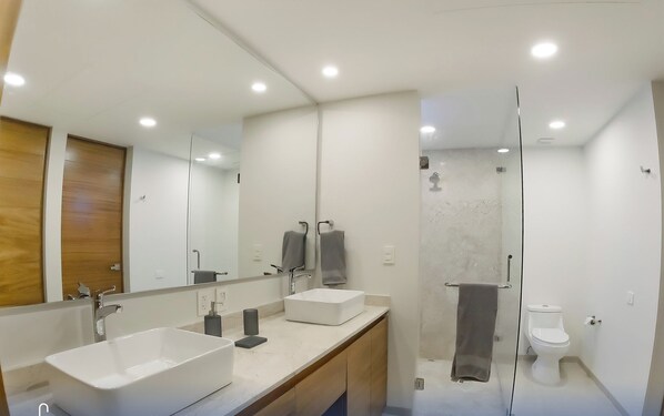 A modern bathroom with two sinks, a large mirror, and a shower area.