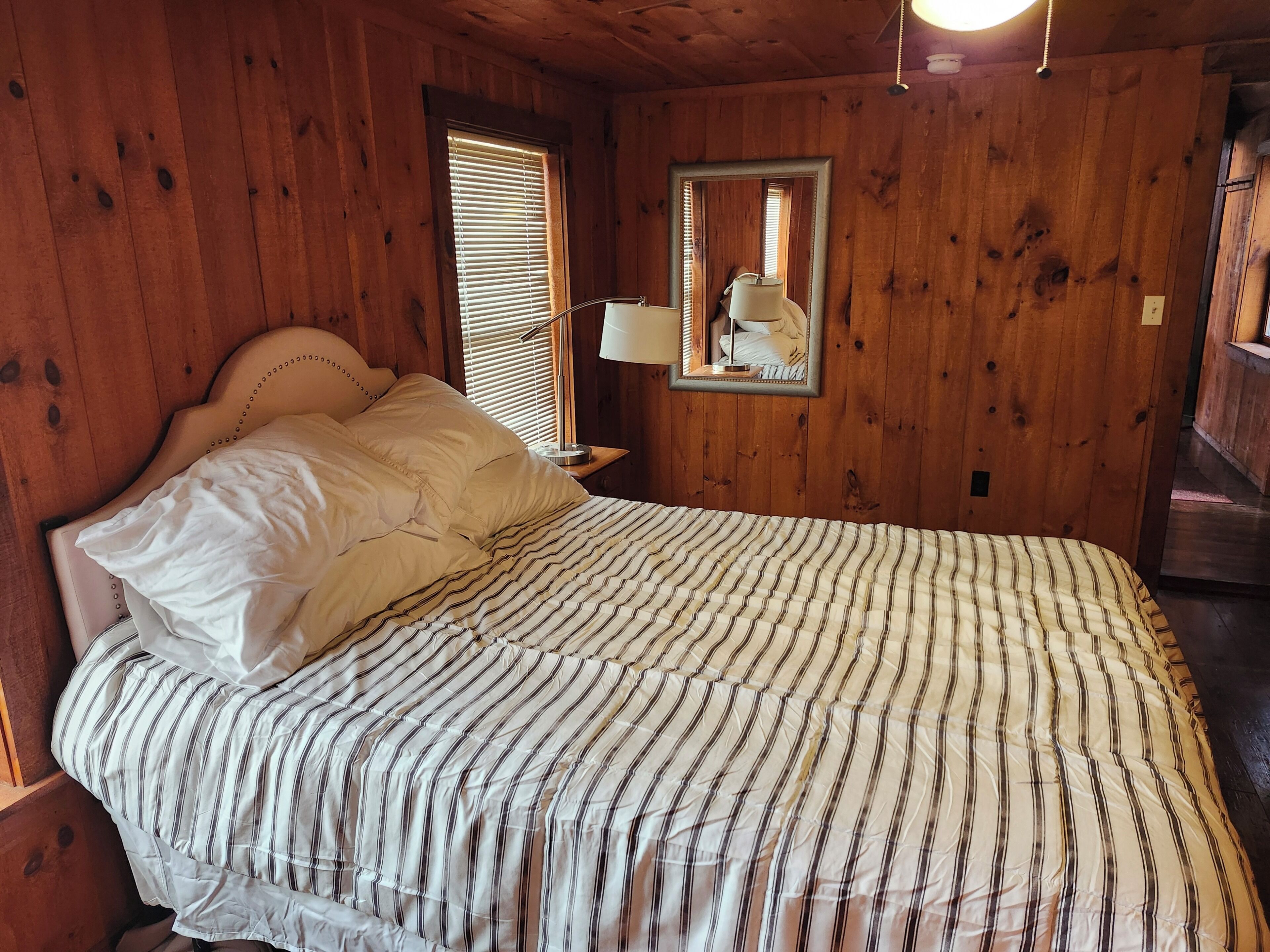 A wooden-paneled room with a bed, a nightstand, a lamp, and a mirror.