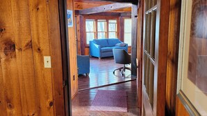 A wooden interior with a door leading to a room with a blue sofa and a chair. - Cabin in the Woods (Franklin)