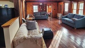 A cozy cabin interior with wooden walls, a sofa, a loveseat, and a television. - Cabin in the Woods (Franklin)