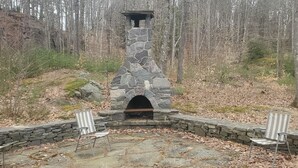 A stone fireplace with two chairs in a forested area. - Cabin in the Woods (Franklin)