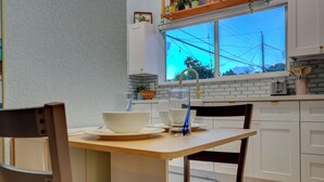 Keittiössä on valkoiset kaapit, ikkunasta avautuu näkymä sähkölinjoille, siellä on leivänpaahdin ja ikkunalaudalla kasvi.