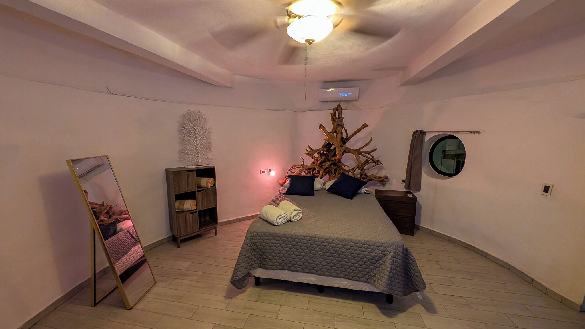 A bedroom with a bed, a mirror, a wooden shelf, a tree branch decoration, and a round mirror on the wall.