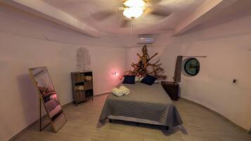 A bedroom with a bed, a mirror, a wooden shelf, a tree branch decoration, and a round mirror on the wall.