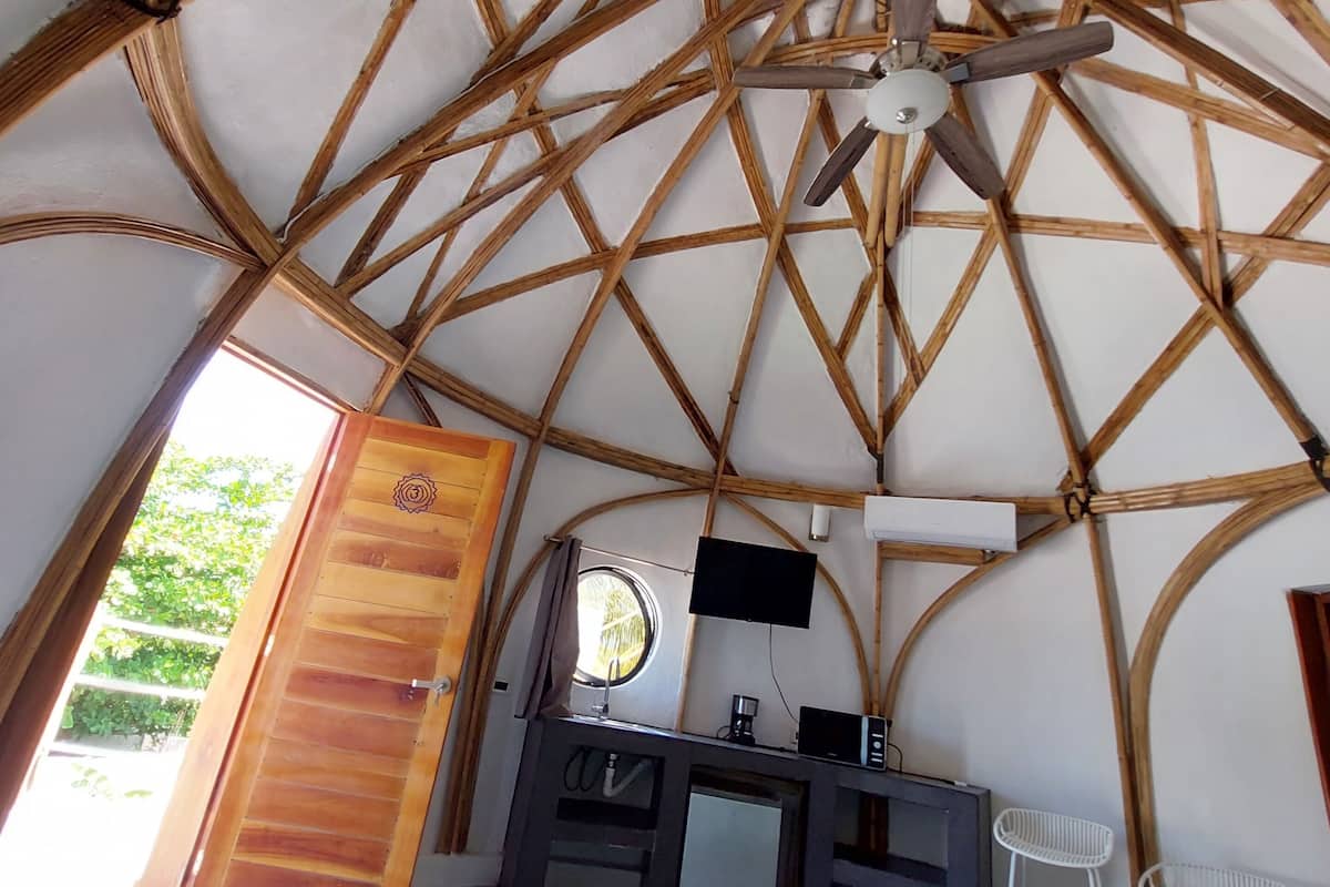Ein Zimmer mit einer hohen Holzbalkendecke, einem Bett, einem Fernseher, einem Schreibtisch und einem Fenster.