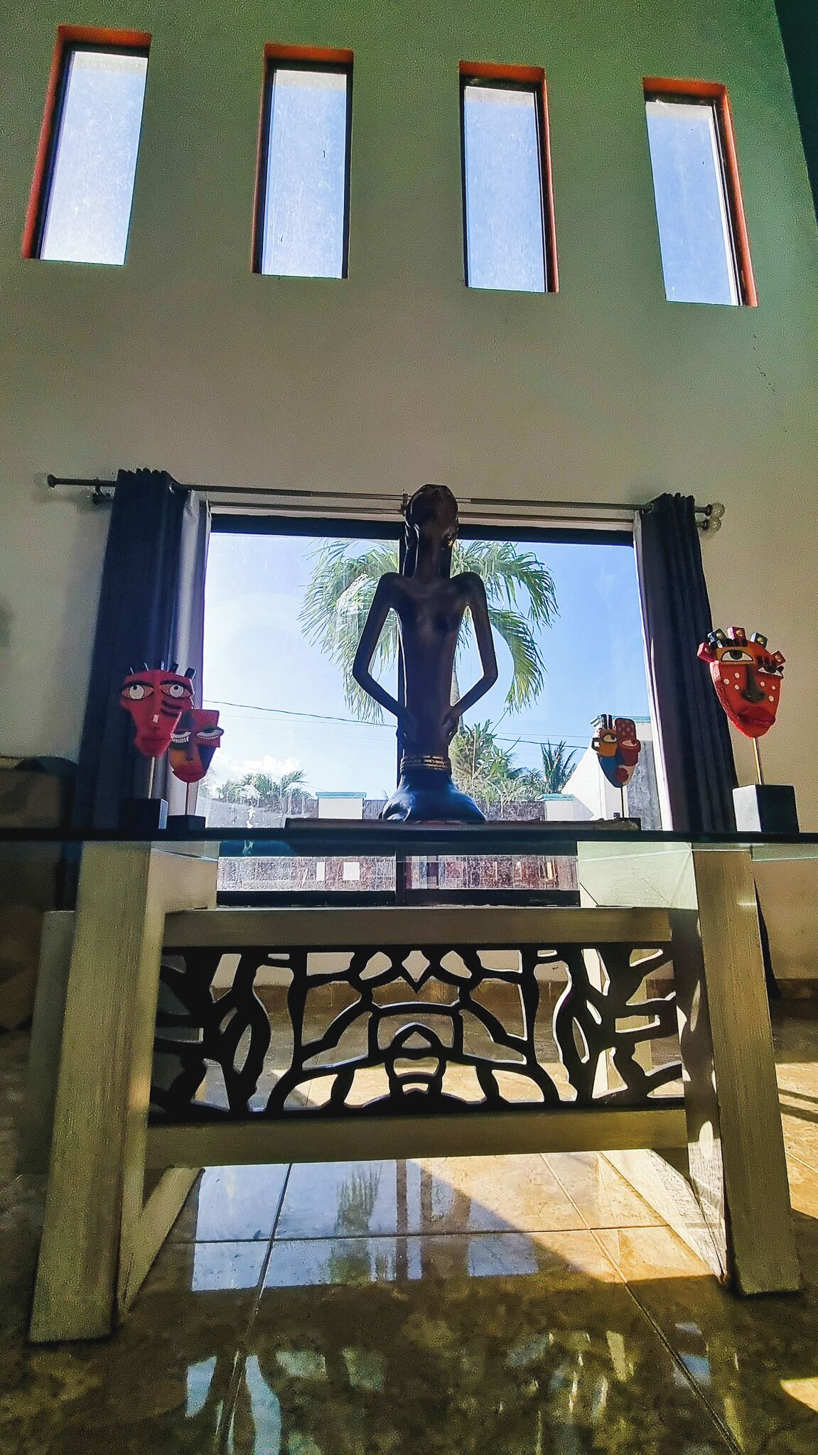 A statue on a balcony with a view of palm trees and a clear sky.