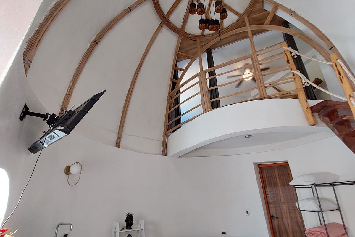 Ein Loft-Zimmer mit hohen Decken, einer Wendeltreppe aus Holz, einer Couch, einem weißen Sessel, einem kleinen Tisch und einer Pendelleuchte.