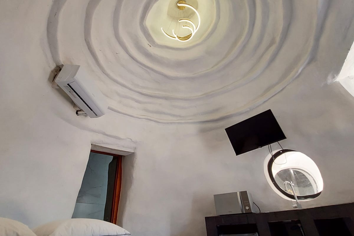 Ein Zimmer mit einem einzigartigen, kreisförmigen Deckenstil, einem Bett mit strukturierter Bettdecke, einem Flachbildfernseher und einem kleinen Fenster.