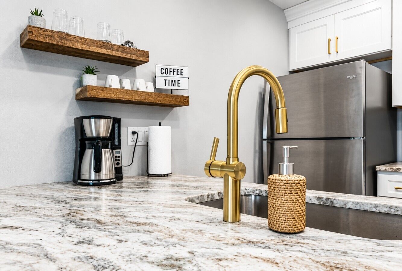 A kitchen with a stainless steel refrigerator, a coffee maker, a gold faucet, and a sign that reads 'Coffee Time'.