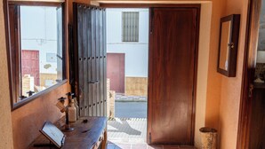 Un corridoio con una porta in legno con l'indicazione SALIDA, uno specchio, un tavolino con una bottiglia e un tappeto sul pavimento.