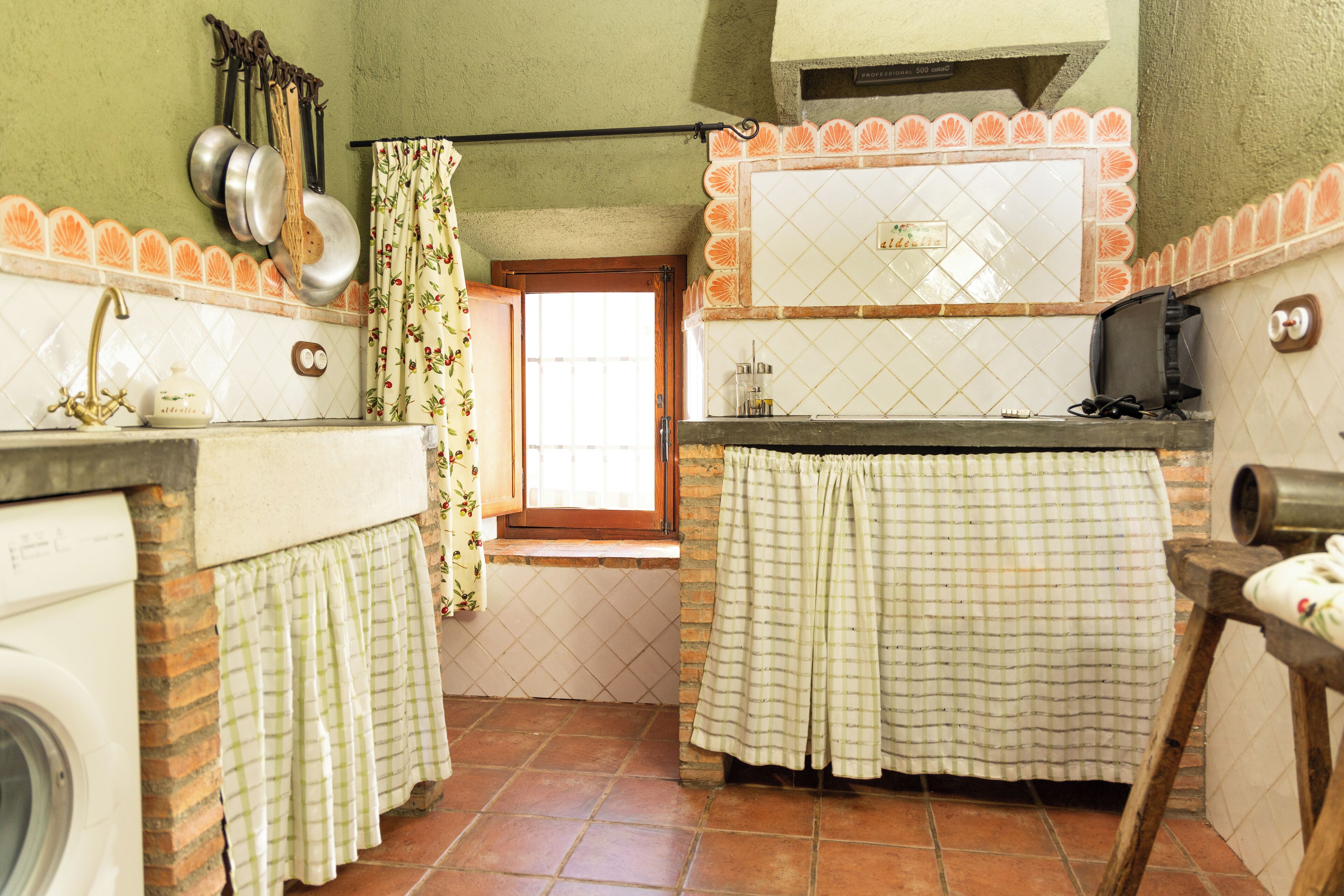 Uma cozinha compacta com máquina de lavar, janela com cortinas e painel de azulejos.