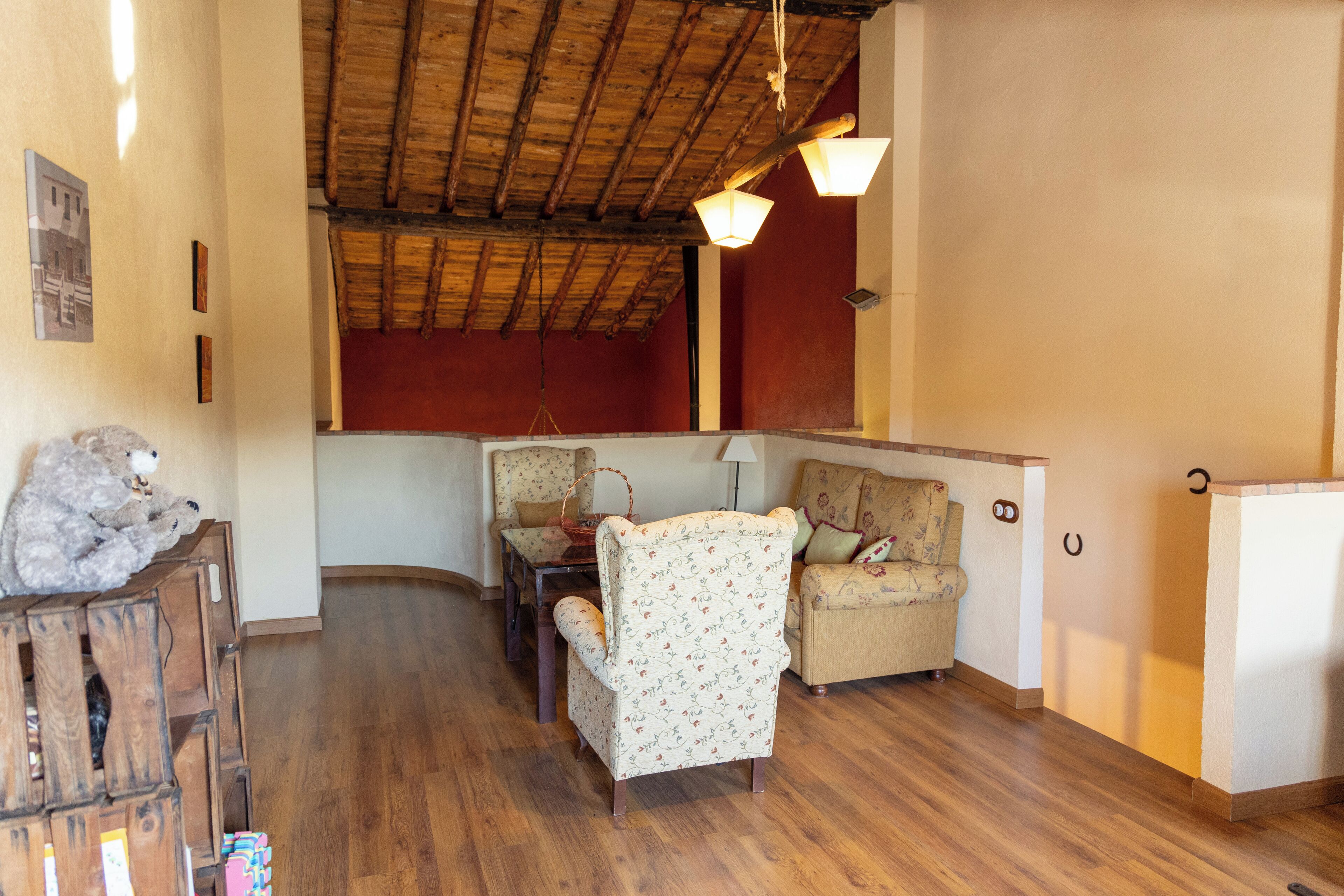 A cozy living room with wooden flooring, a high ceiling with exposed beams, and two upholstered chairs with floral patterns.