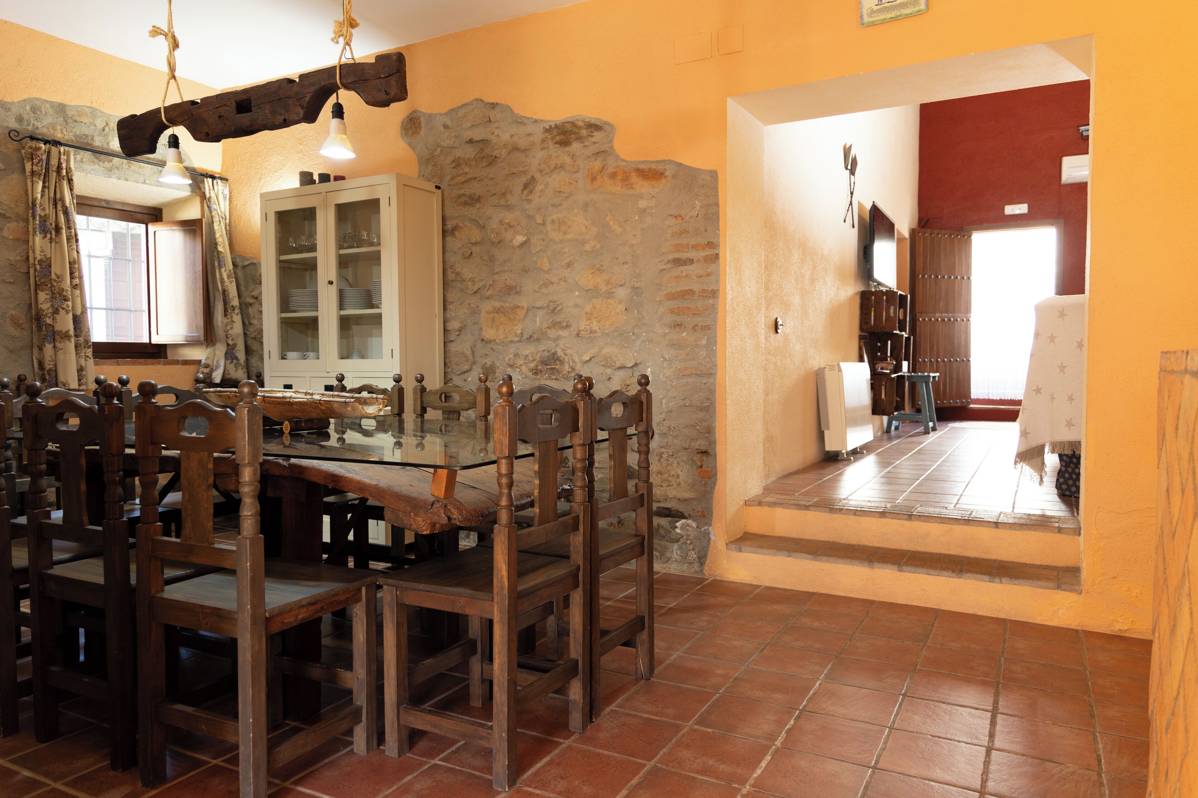 A dining area with a glass table surrounded by wooden chairs, a stone wall, and a cabinet with glass doors.