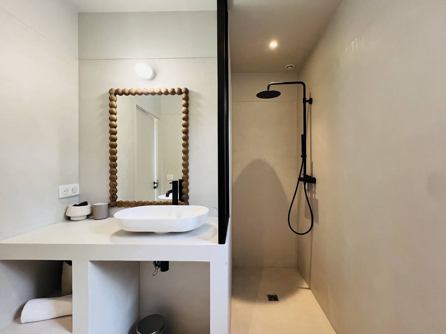 A modern bathroom with a white sink, a large mirror with a unique frame, and a separate shower area.