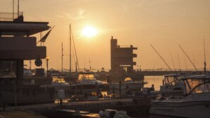 Una marina con imbarcazioni ormeggiate, un edificio con tetto piatto e un grande sole nel cielo.