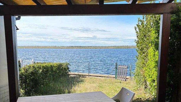 Patio esterno con tavolo e sedie, affacciato su un corso d'acqua e un molo.