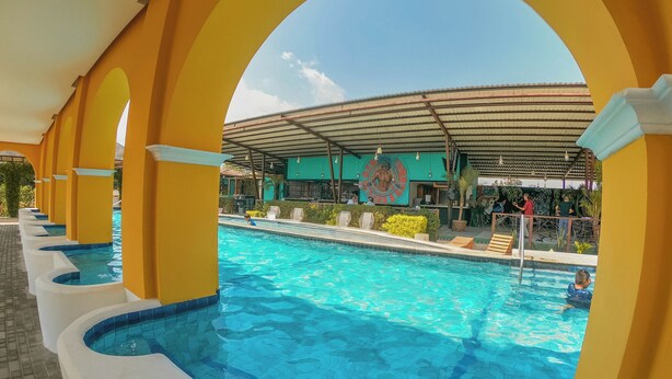 A swimming pool with a tiled deck and a covered area with a mural. - Elite Maya Spa  (Antigua Guatemala)