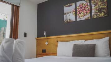 Habitación de hotel con cabecera de madera, ropa de cama blanca y un cuadro de bayas colgado en la pared.