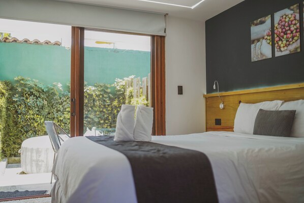 A hotel room with a bed, a view of the garden, and a wooden headboard. - Elite Maya Spa (Antigua Guatemala)