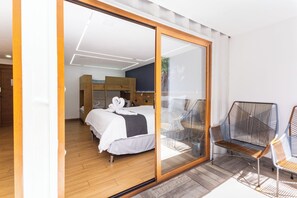 Une chambre moderne dotée d’une grande porte-fenêtre coulissante donnant sur un balcon, d’un lit avec du linge de lit blanc et de deux fauteuils en osier.