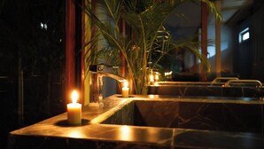 A dimly lit bathroom with a marble sink, a lit candle, and a potted plant. - Elite Maya Spa  (Antigua Guatemala)