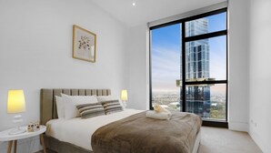 A modern hotel room with a large window, a bed, a bedside table, and a framed picture on the wall.