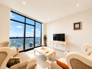 Amplia sala de estar con un gran ventanal, televisor de pantalla plana y muebles elegantes.