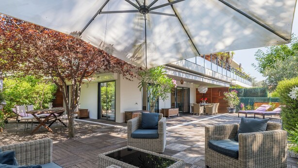 An outdoor patio area with wicker furniture, a large umbrella, and a view of a modern building.
