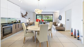 A modern kitchen with a dining area, featuring a round table, chairs, and a large window with a view of greenery.