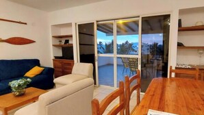 A living room with a blue sofa, a wooden dining table, and a sliding glass door leading to a balcony. - Waterfront retreat in Casablanca (Same)