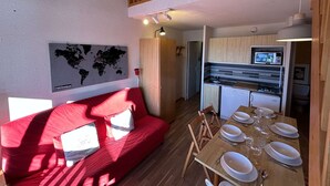 Un ambiente compatto con un divano rosso, un tavolo da pranzo per quattro persone, una zona cucina con forno a microonde e una mappa del mondo appesa al muro.