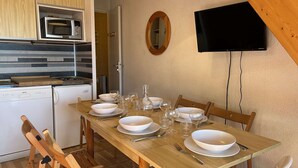 Zona pranzo con tavolo in legno apparecchiata per quattro persone, forno a microonde, piccolo frigorifero e televisore a parete.