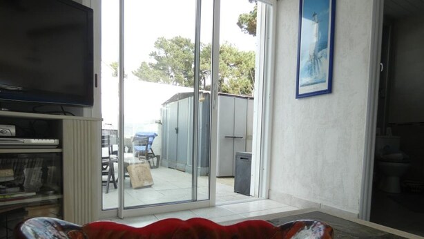 A room with a large glass door leading to an outdoor area, a television on the left, and a red decorative bowl in the foreground. - House in Fromentine 65m², 4 pers, close to beach, parking (La Barre-de-Monts)