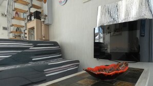 A living room with a striped sofa, a flat-screen TV mounted on the wall, and a decorative bowl on a tiled floor. - House in Fromentine 65m², 4 pers, close to beach, parking (La Barre-de-Monts)