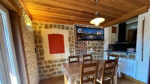 A dining area with a wooden table and chairs, a stone wall, and a kitchen in the background.