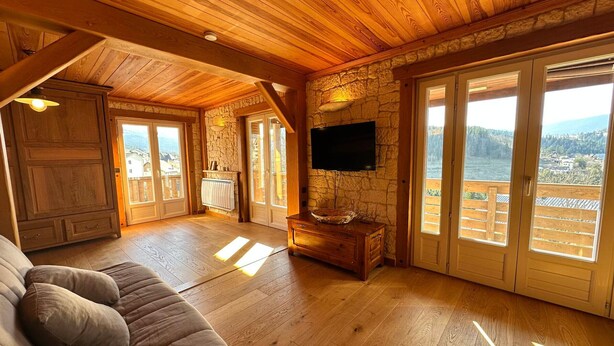 A spacious living area with wooden flooring, a sofa, a stone wall, and a television.
